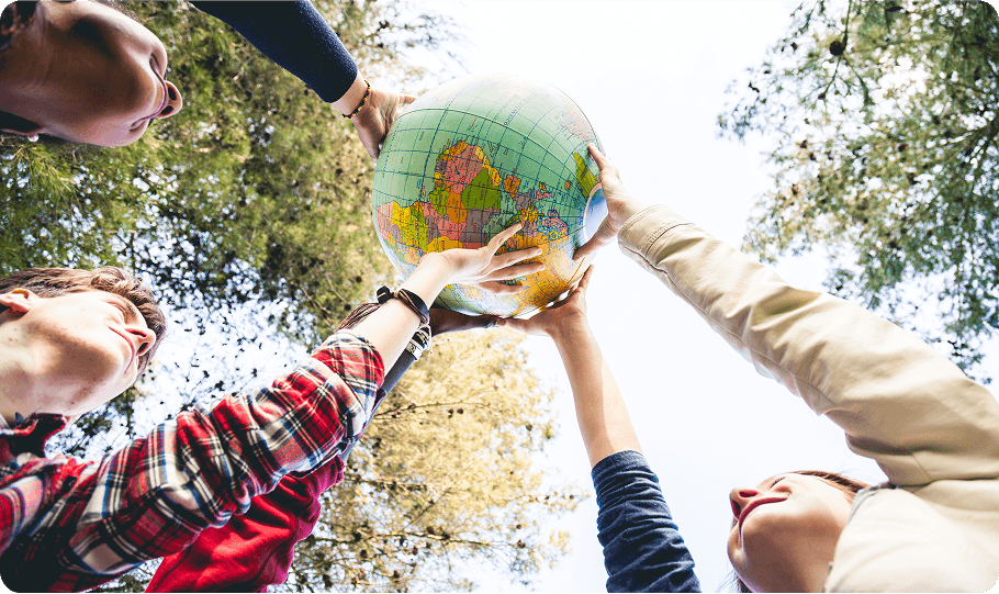 People holding a globe outdoors, looking upwards.