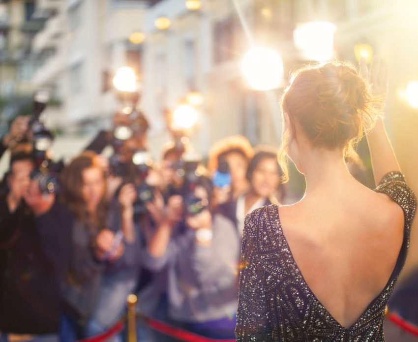 Celebrity waving to paparazzi on red carpet.